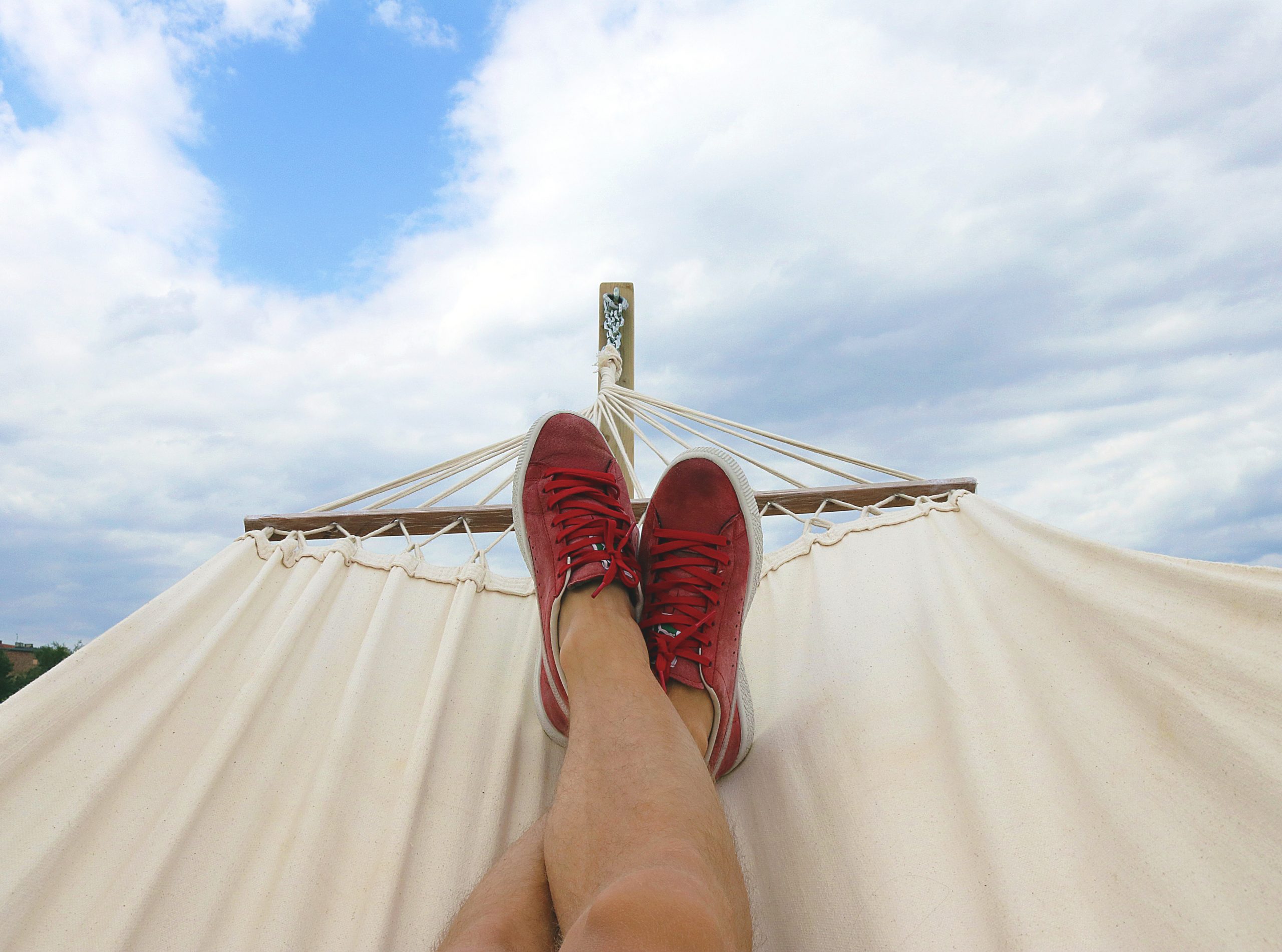 legs and feet with red shoes laying in a hammock with blue skies in the background